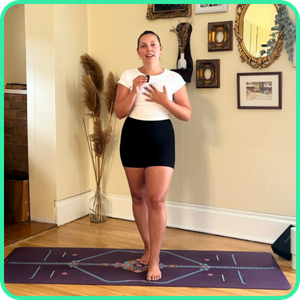 Video thumbnail for a 30 minute standing full body yoga class, woman standing on a yoga mat with hand on chest in a plant-filled room
